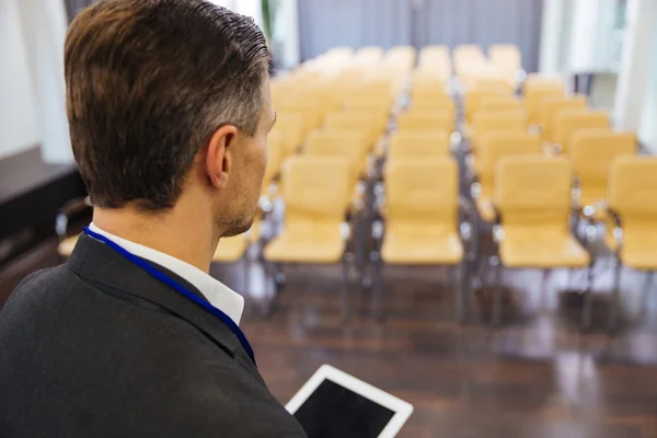 Businessman holding tablet in empty conference hall — Stock Photo, Image
