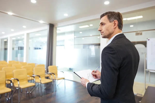 Businessman with clipboard standing in empty conference hall — Stock Photo, Image