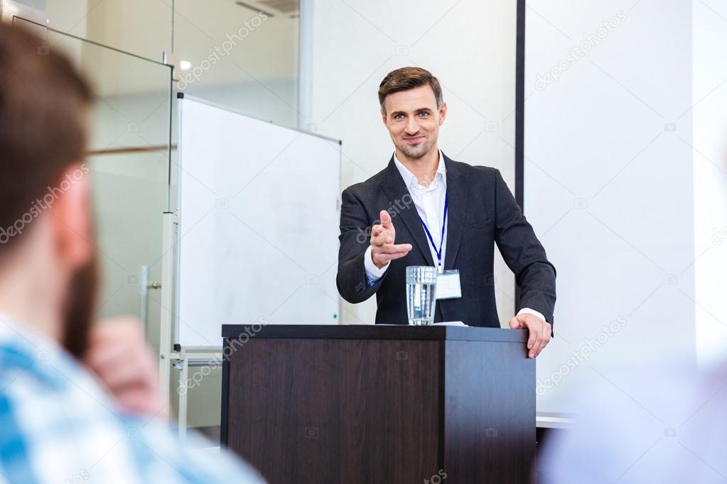 Smiling businessman standing at tribune in conference hall 