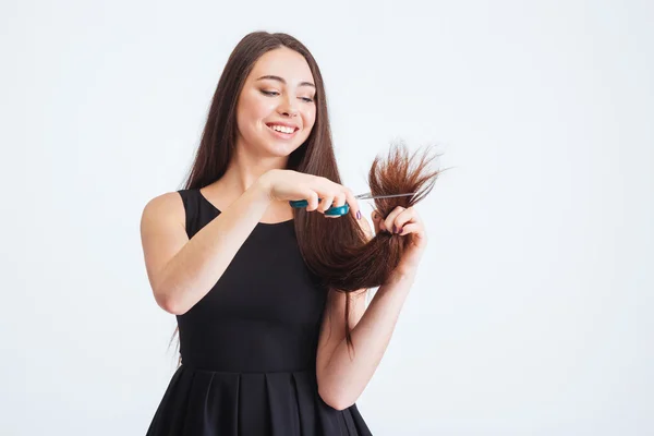 Sorrindo bela mulher cortando pontas de divisão de cabelo com tesoura — Fotografia de Stock