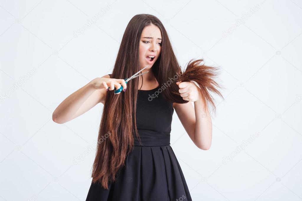 Shocked unhappy woman trimming split ends of hair with scissors 
