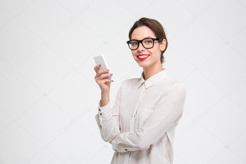 Cheerful attractive businesswoman in glasses standing and using mobile phone