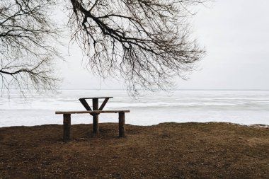 Donmuş nehrin yanındaki parkta tahta masa ve bank.