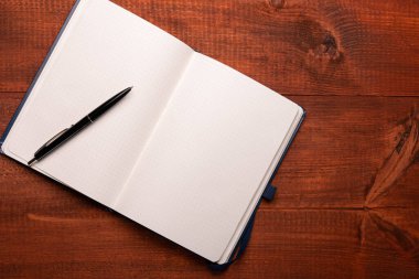 Ahşap bir masanın üzerinde bir kalemle defteri aç