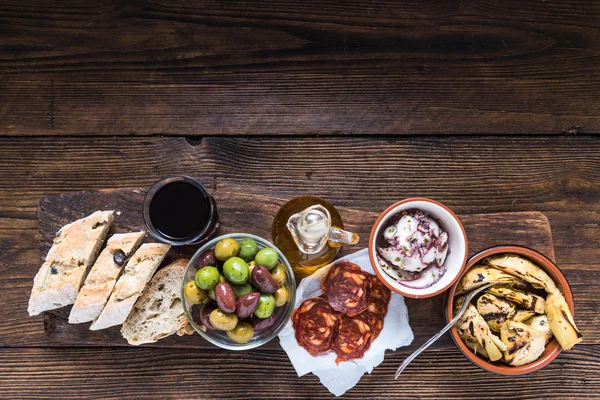 Wooden board with tapas, olives and salami and olive oil — Stock Photo, Image