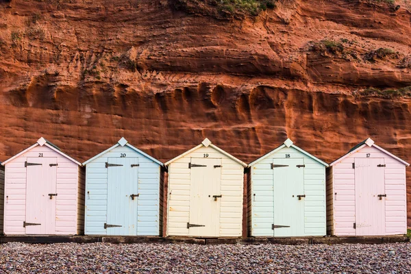 Rangée de cabane de plage aux couleurs pastel, fond rocheux rouge — Photo