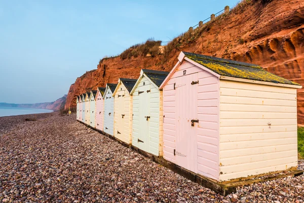 Beach hut row in pastel colors, red rock cliff background — Stock Photo, Image