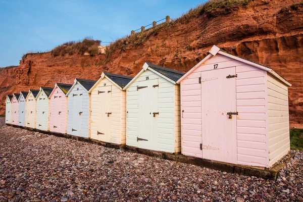 Beach hut row in pastel colors, red rock cliff background — Stock Photo, Image