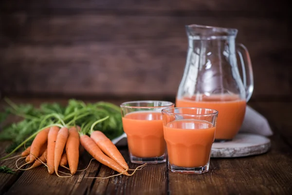 Свежий морковный сок в банке и стаканах — стоковое фото