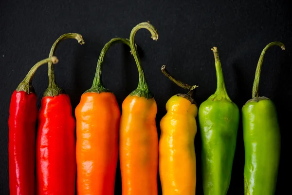 Vibrant colors on peppers on black slate bacground — Stock Photo, Image