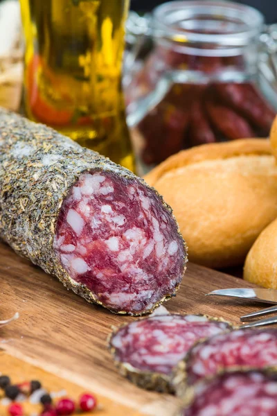 Traditional salami with herbs on wooden board and olive oil — Stock Photo, Image
