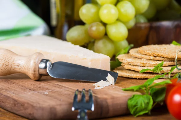 Parmesan cheese on board with grapes and basil — Stock Photo, Image