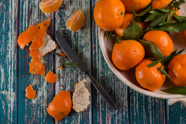 Pelar clementinas recién recogidas con cuchillo en mesa rústica — Foto de Stock