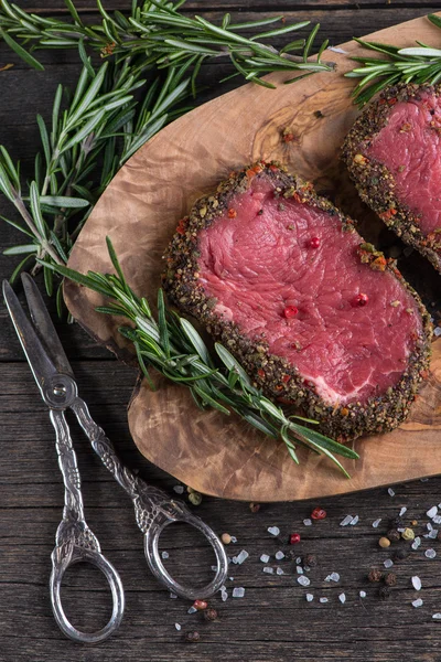 Raw peppered steak with herbs on wooden table — Stock Photo, Image