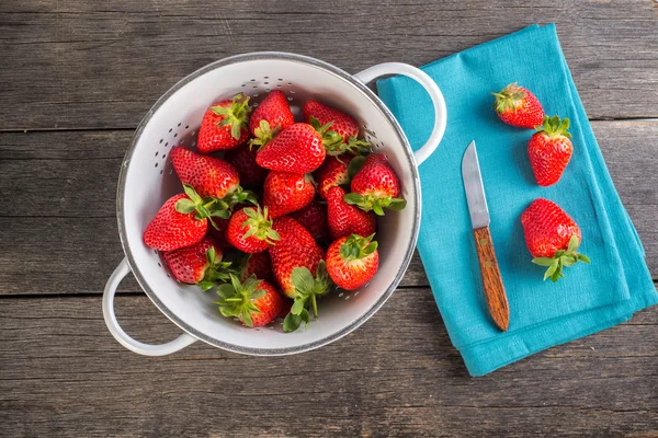 Verse aardbeien in rustieke vergiet op houten tafel — Stockfoto