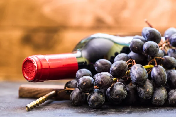 Botella de vino tinto y uvas sobre fondo de madera — Foto de Stock