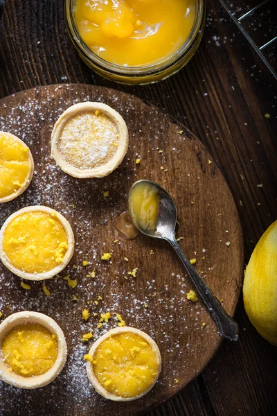 Riempimento di mini crostate di limone e crema pasticcera su tavola di legno — Foto Stock