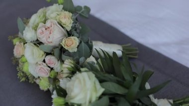 Gri kapaklı bir yatakta uzanan güzel beyaz güllerden yapılmış üç düğün buketinin yakın çekimi. Yavaşça.