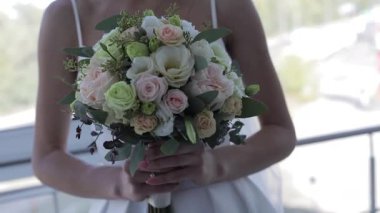 Gelinin düğün elbisesinin yakın çekimi, elinde lüks bir buket tutarken ve nazikçe yüzüklü elini üzerinden geçirirken. Güller, şakayıklar