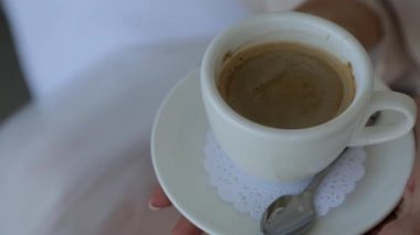 Espresso kahvesiyle dolu beyaz bir fincanı tutan bir kadın eli. Sıcak bir sabah atmosferi