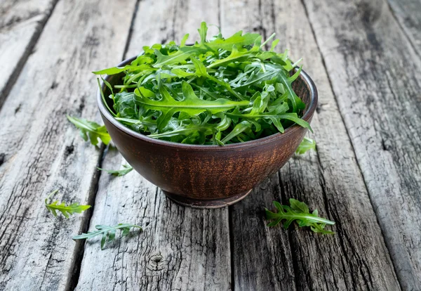 Fresh rucola in a bowl on a rustic wooden table. — Stock Photo, Image