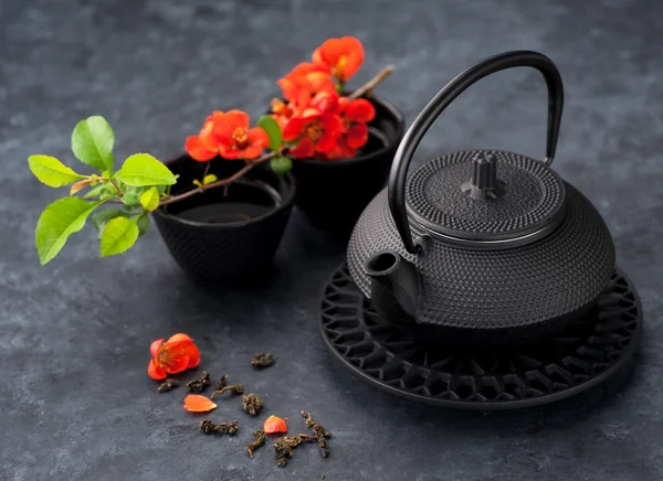 Black iron asian style teapot and cup green tea and flowers on black grunge background