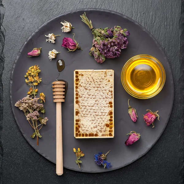 Honey and dried herbs on dark background