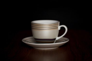 Kupası ve fincan tabağı çizgili koyu arka plan üzerinde ahşap bir masa üzerinde duran