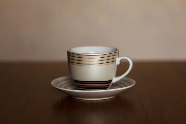 Cup and saucer with stripes standing on a wooden table on a dark background — Stock Photo, Image