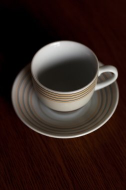 Kupası ve fincan tabağı çizgili koyu arka plan üzerinde ahşap bir masa üzerinde duran