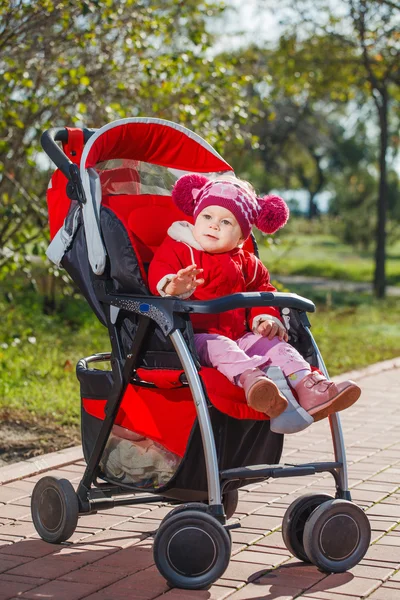 Beautiful little girl in a red jacket on the pram in park Stock Picture