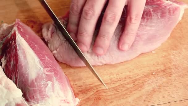 Close-up man in the kitchen is cutting pork on cutting board — Stock Video