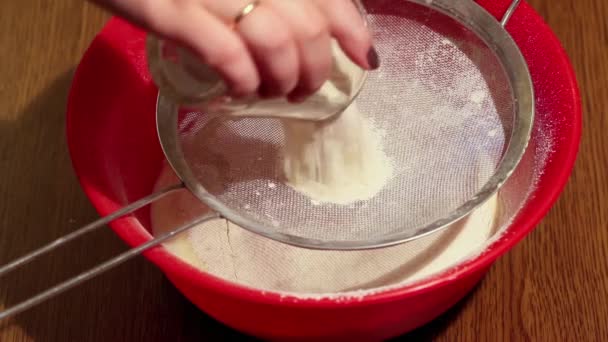 Donna usa un setaccio per setacciare la farina in una ciotola di plastica su un tavolo di legno, primo piano — Video Stock