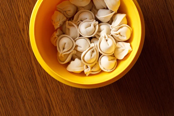 Fresh frozen ravioli in a yellow plate standing on a wooden table — Stock Photo, Image