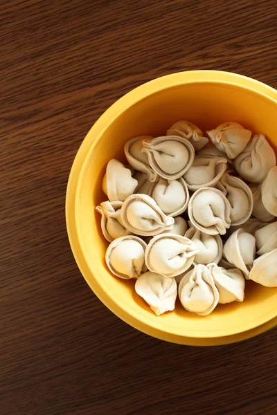 Ravioli congelados frescos em uma placa amarela que está em uma mesa de madeira — Fotografia de Stock