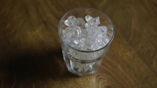 Vidro com gelo gira em torno do eixo na mesa de madeira — Vídeo de Stock