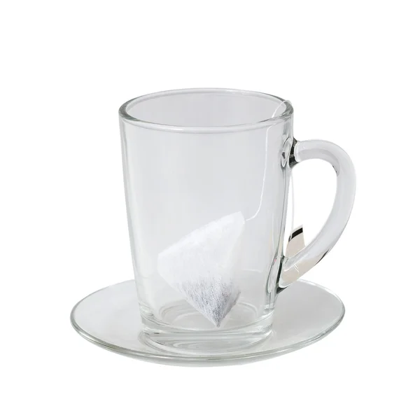 Copo de vidro e pires com saco de chá no fundo branco — Fotografia de Stock