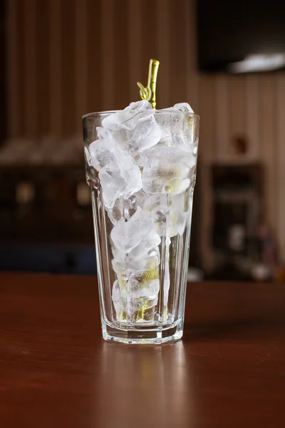 Highball glass with ice and a yellow tube on the wooden bar — Stock Photo, Image