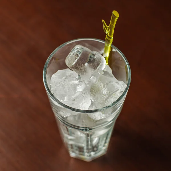 Highball glass with ice and a yellow tube on the wooden bar — Stock Photo, Image