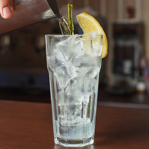 Verre highball avec glace et un tube jaune sur la barre en bois — Photo