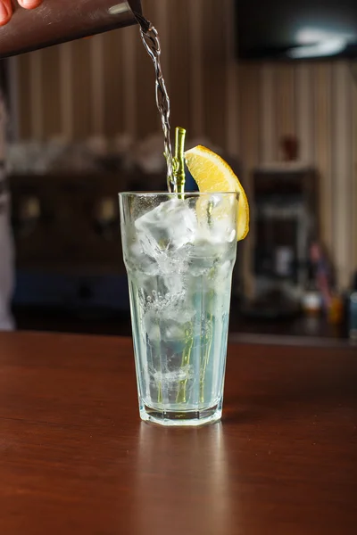 Highball glass with ice and a yellow tube on the wooden bar — Stock Photo, Image