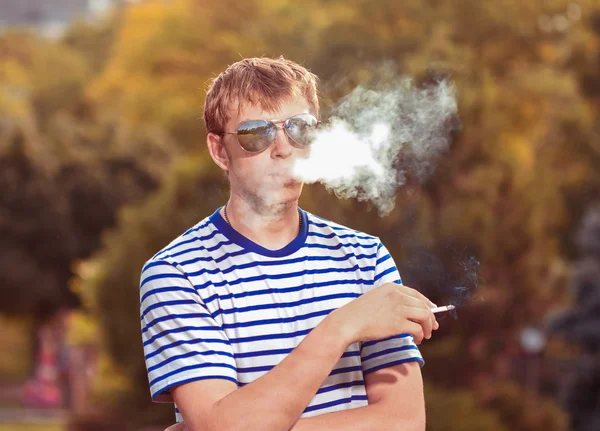 Hipster beau jeune homme avec une cigarette gros plan sur un backgr — Photo