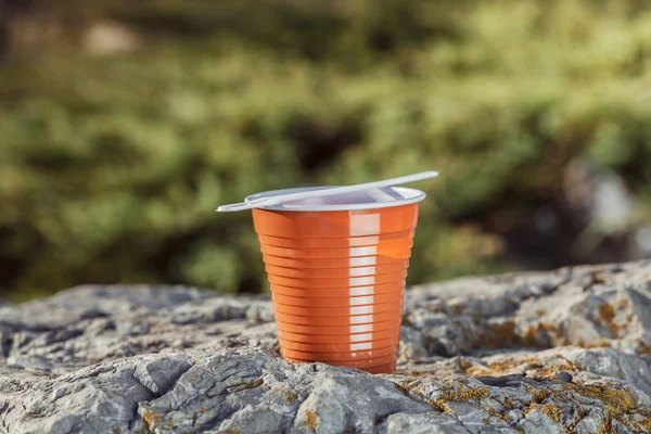 Tazza di caffè di plastica marrone con un cucchiaio su una roccia su uno sfondo — Foto Stock