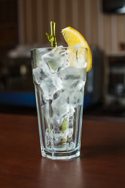 Verre highball avec glace et un tube jaune sur la barre en bois — Photo