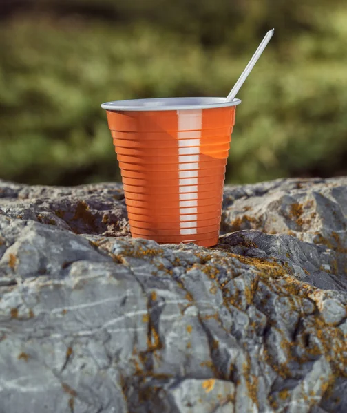 Tazza di caffè di plastica marrone con un cucchiaio su una roccia su uno sfondo — Foto Stock