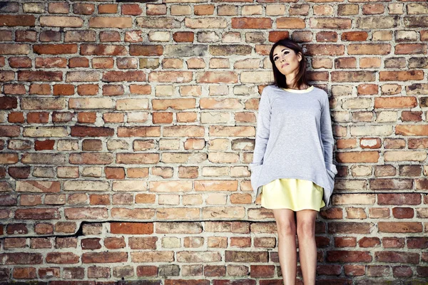 Pensive woman against a brick wall — Stock Photo, Image