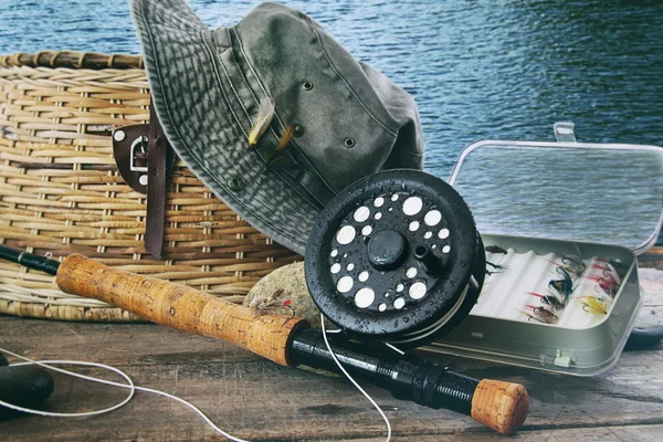 Sombrero y artes de pesca con mosca en la mesa cerca del agua —  Fotos de Stock