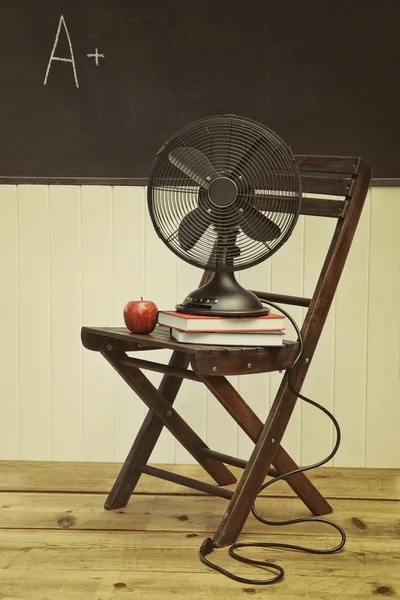Старый веер с яблоком и книгами на стуле — стоковое фото