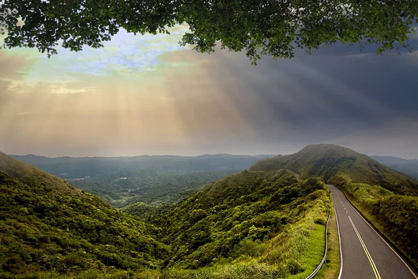 美しい夕日と山と雲と空の背景に山の頂上に沿って道路の輪郭上の太陽光線 — ストック写真