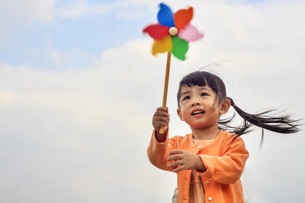 Cute little girl on grass in summer day holds windmill — Stock Photo, Image